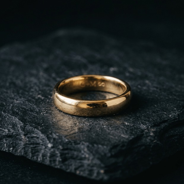 Smooth gold wedding band on dark textured stone surface