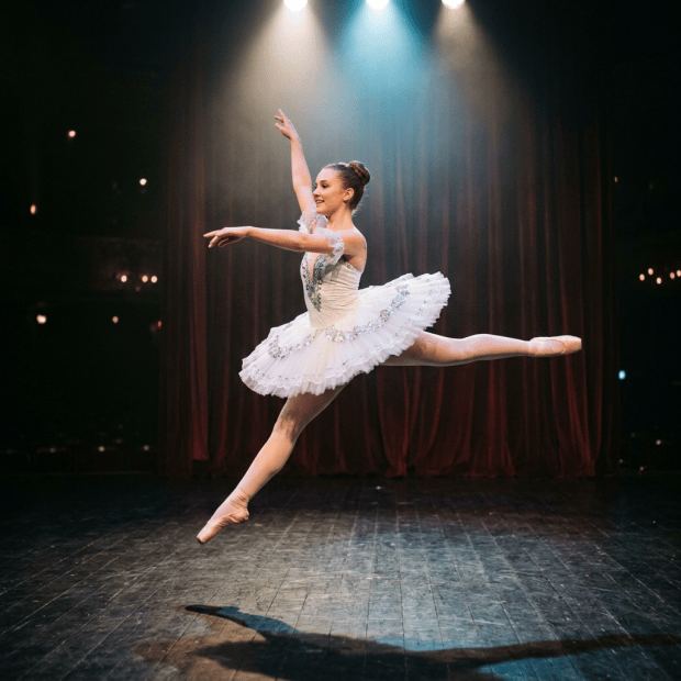 Ballerina in mid-air performing a leap with a white tutu on a theater stage